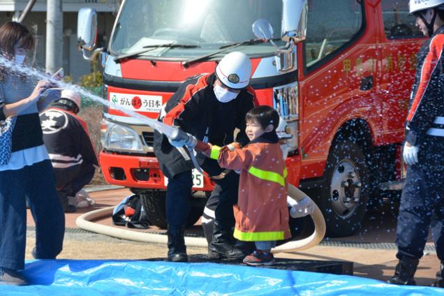 島上条公園にて男の子が甲斐市消防団員と一緒に放水体験している写真